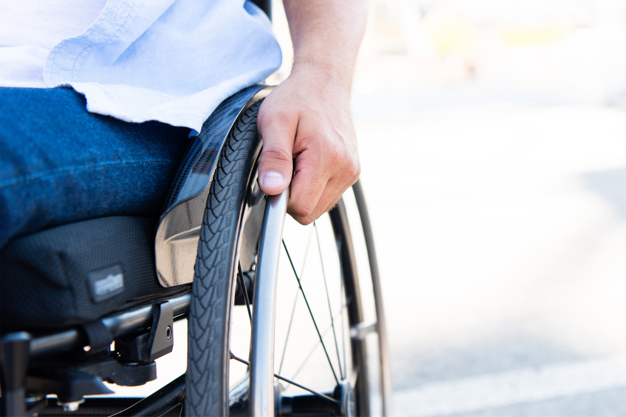 Zdjęcie osoby poruszającej się na wózku, zbliżenie na koło wózka.