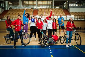 Grupa czternastu studentów na sali sportowej, w sportowych ciuchach, z rowerami.