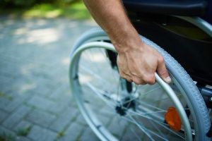 Zbliżenie na rękę trzymającą koło wózka inwalidzkiego.