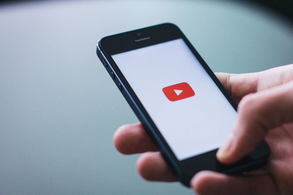 Smartfon trzymany w dłoni, na ekranie widoczne logo YouTube.